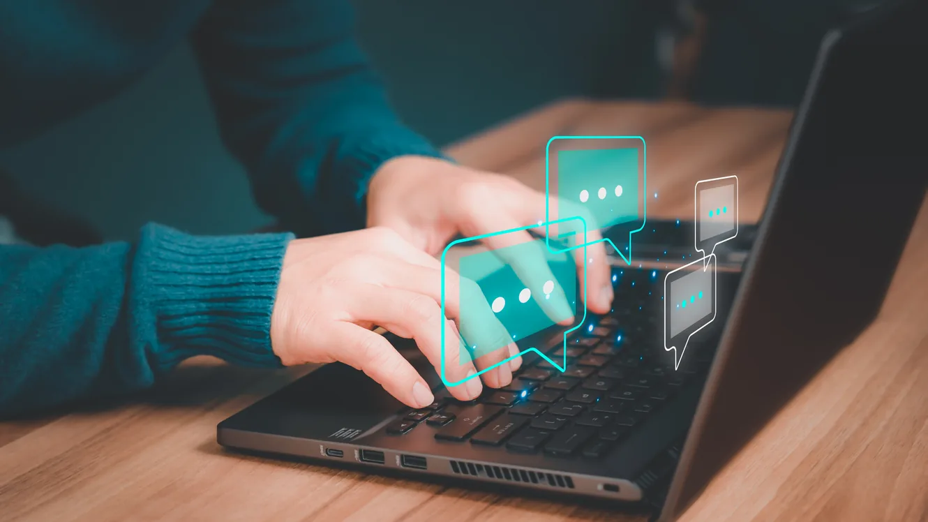 Hands typing on a laptop surrounded by glowing chat bubbles
