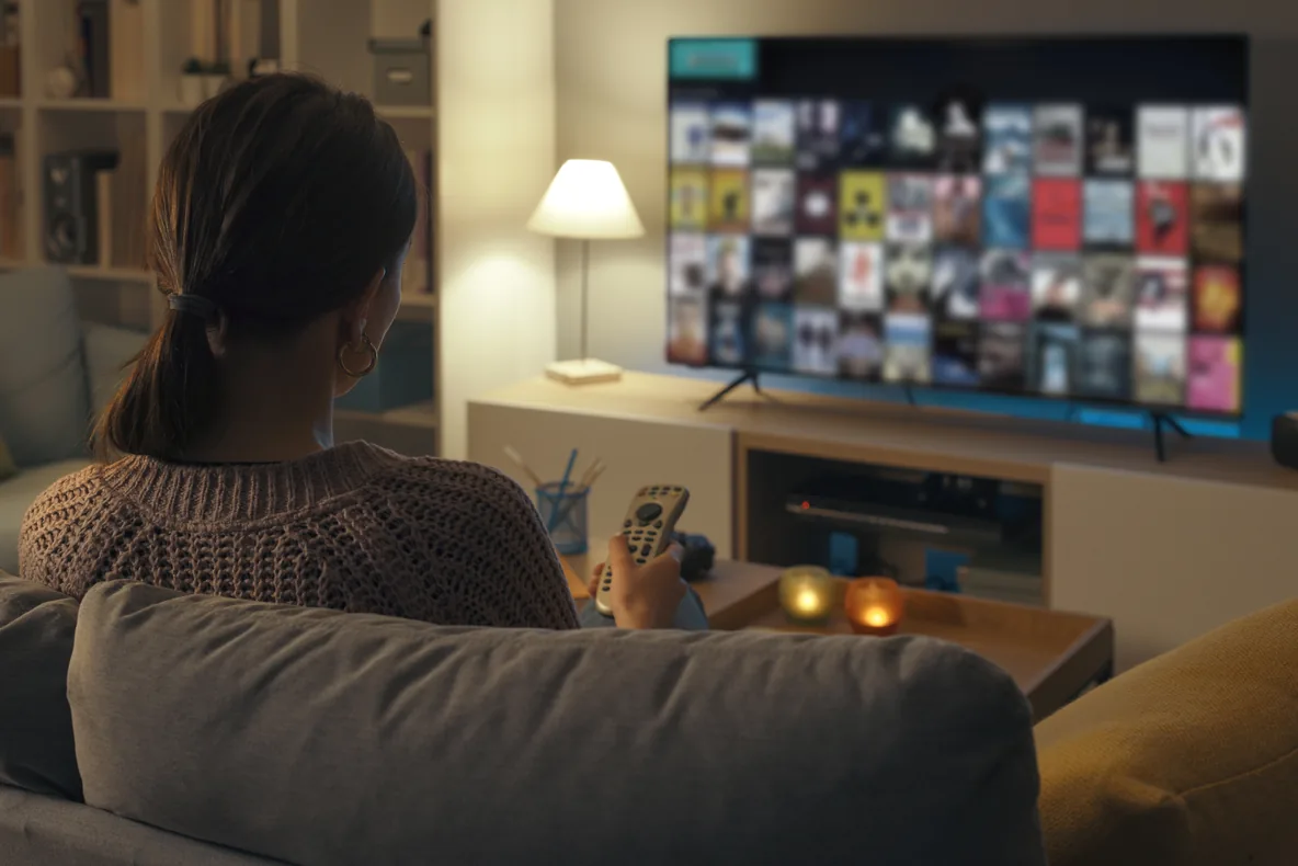 A woman on a sofa browses a streaming library on her TV