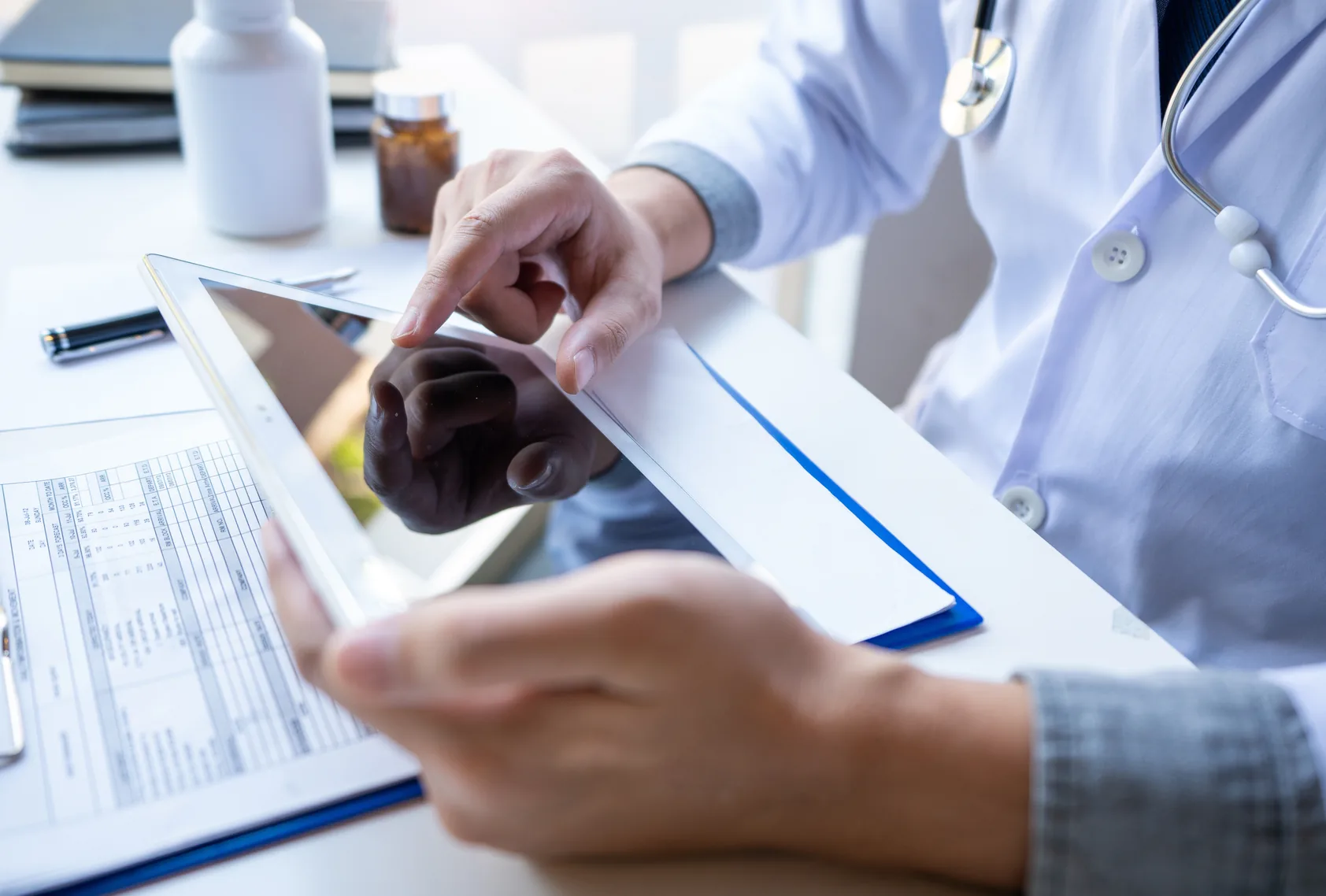 A doctor taps a tablet beside a clipboard holding a billing form