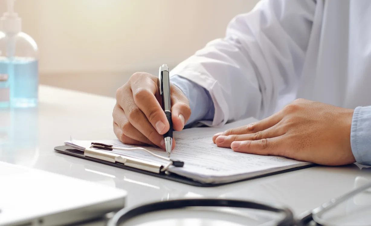 A doctor fills in a form on a clipboard