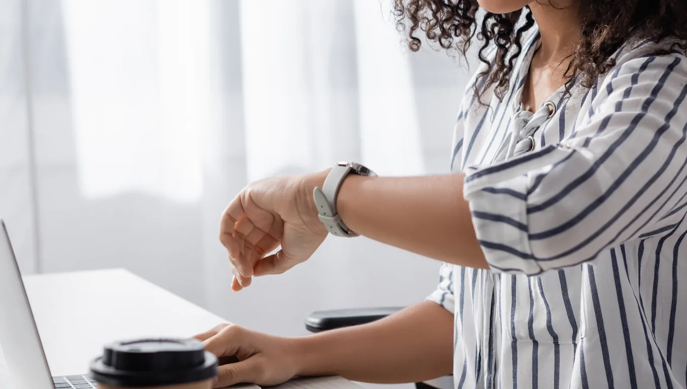 A woman checks her wristwatch at her desk